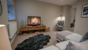 Ein gemütliches Wohnzimmer mit Fernseher, Kamin, Sessel und Sofa.
