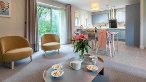 Ein modernes Wohnzimmer mit einer Couch, einem Sessel, einem Esstisch mit Schüsseln Frühstücksflocken und einer Vase mit Blumen.