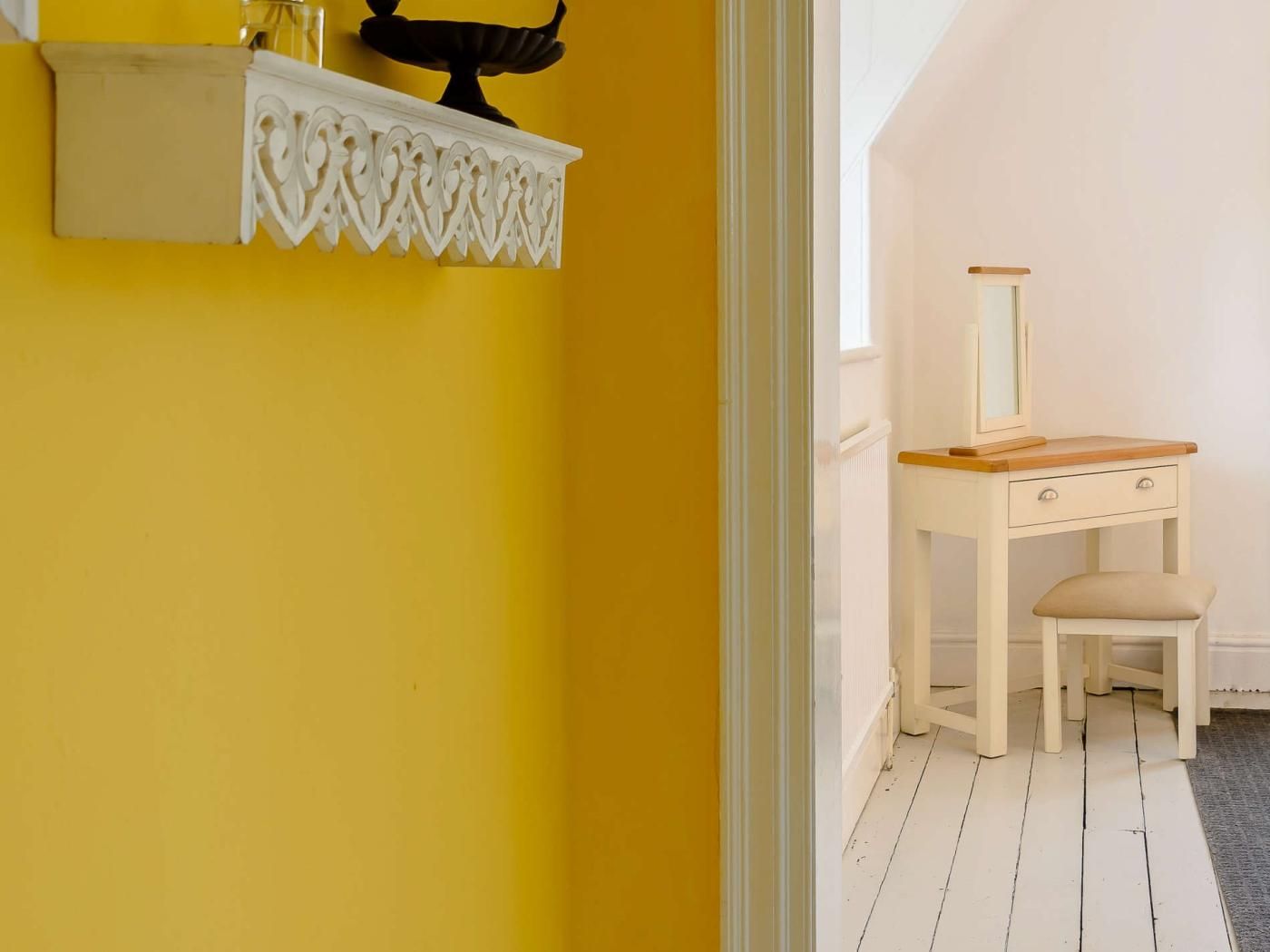 Ein Zimmer mit gelber Wand, einem weißen Schminktisch mit Spiegel und einem kleinen Stuhl.