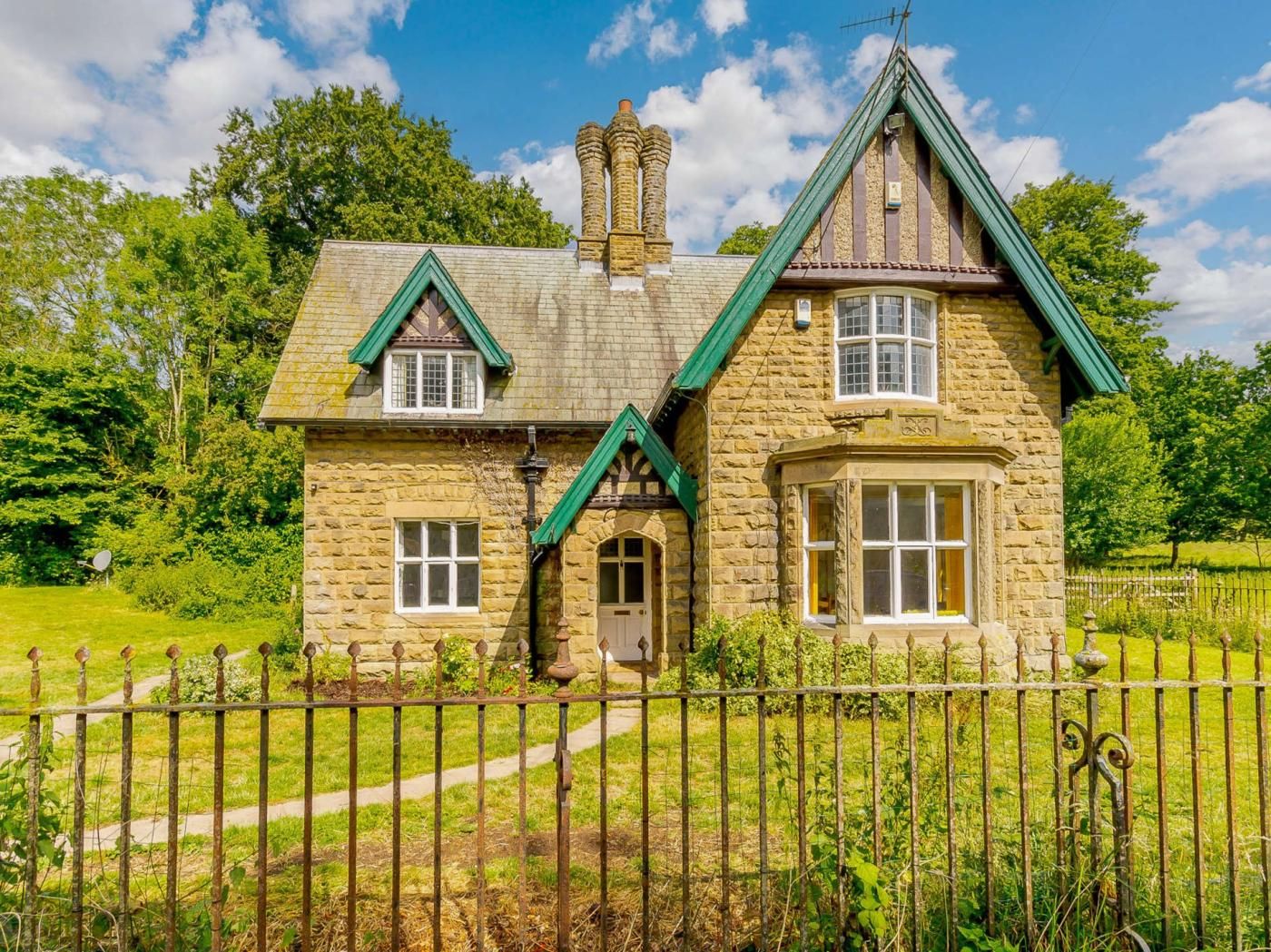A stone house with a green roof, a chimney, and a fenced yard.