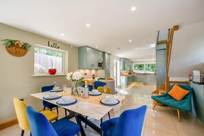 A modern kitchen with a dining area, featuring a large island, blue chairs, and a 'hello' sign on the wall.