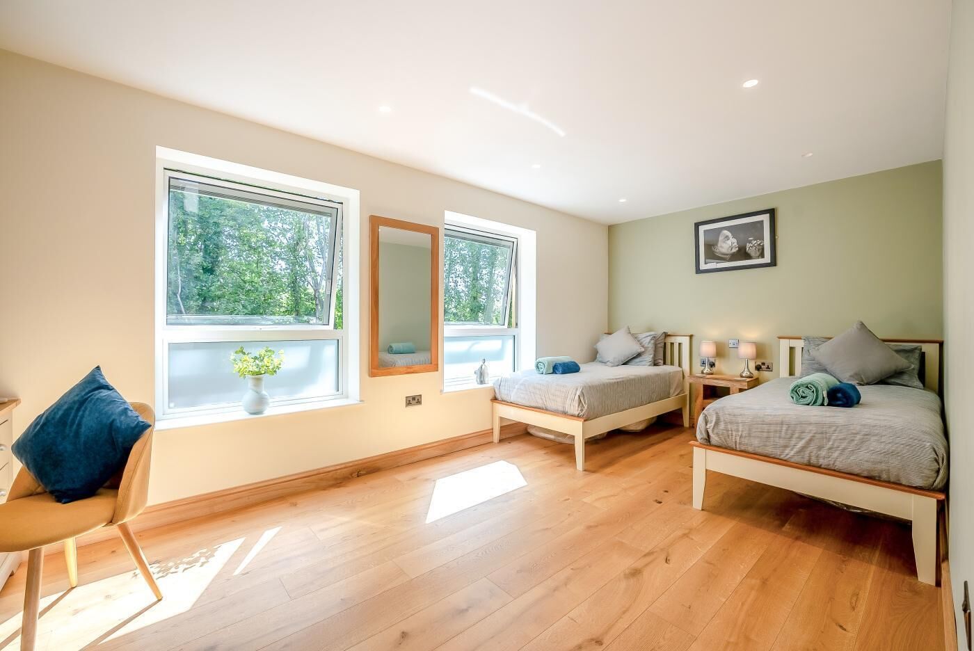 A bedroom with two beds, a chair, a mirror, and large windows.
