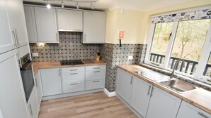A kitchen with light grey cabinets, a wooden countertop, a built-in stove, and a window with a view of trees. - 3 Bed in Ambleside (oc-87524) (Ambleside)
