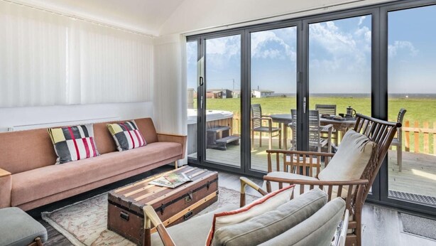Un salón amplio con un gran ventanal corredera que da a un patio exterior, un sofá acogedor, una mesa de centro de madera y un sillón cómodo.