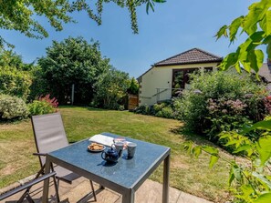 A patio with a table set for tea, surrounded by a well-maintained garden and a house in the background.