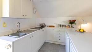 Een praktische keuken met witte keukenkastjes, een spoelbak, een broodrooster en een klein aanrecht met een fruitschaal.