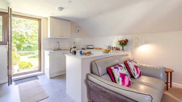 Een moderne keuken met witte kastjes, een centraal eiland en een zithoek met een bank en decoratieve kussens.