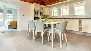 A modern kitchen with wooden ceiling, white cabinets, and a dining area with a table and chairs. - 3 Bed in Saltash (oc-87717) (Saint Mellion)
