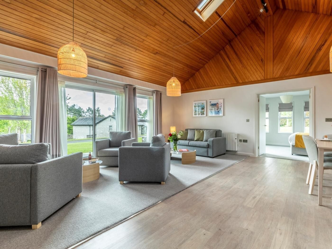 A spacious living area with a high wooden ceiling, large windows, and a dining area.