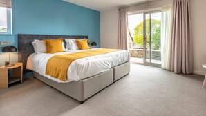 A bedroom with a bed, a nightstand, a lamp, and a view of the outdoors through a sliding glass door. - 3 Bed in Saltash (oc-87717) (Saint Mellion)