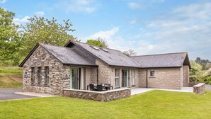 A stone house with a patio, large windows, and a grassy lawn. - 3 Bed in Saltash (oc-87717) (Saint Mellion)