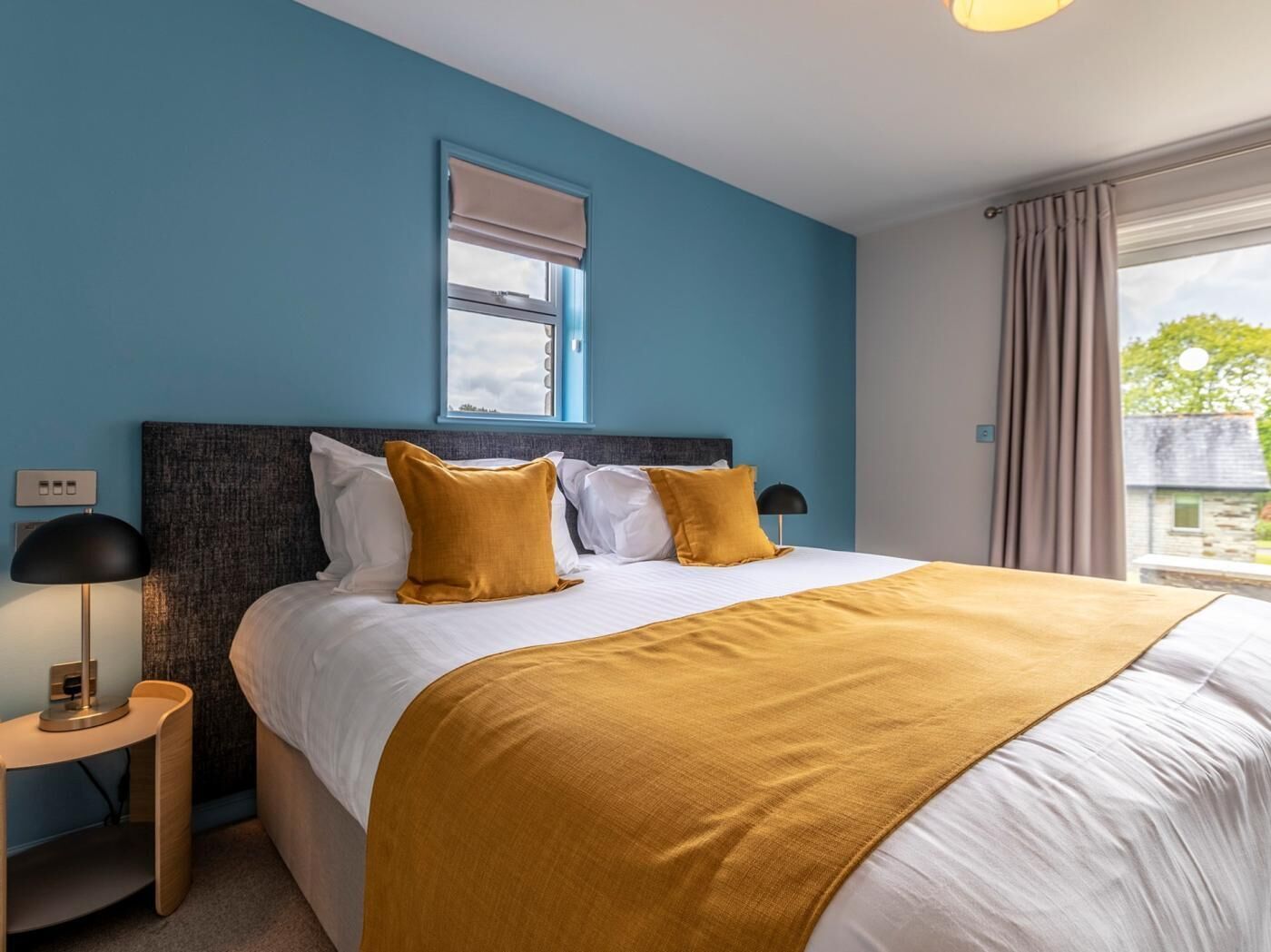 A bedroom with a bed, bedside tables, a window, and a view of the outside.