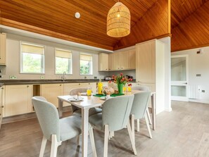 Une cuisine moderne avec un plafond en bois, des armoires blanches et un coin repas avec des chaises grises.