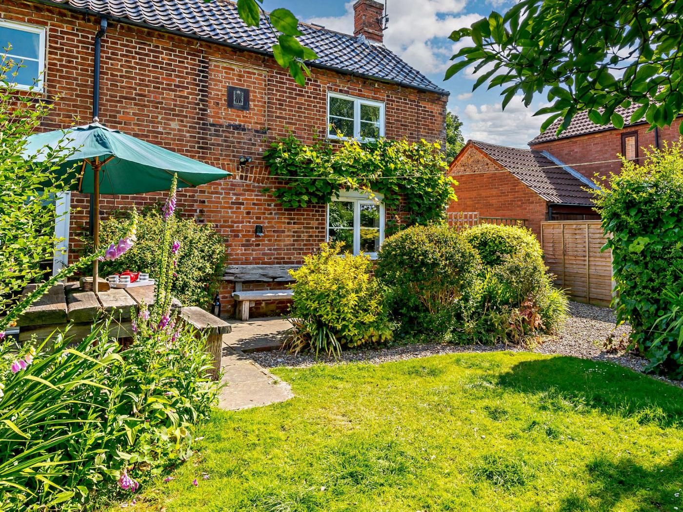 A brick house with a garden, a wooden fence, and a green umbrella.