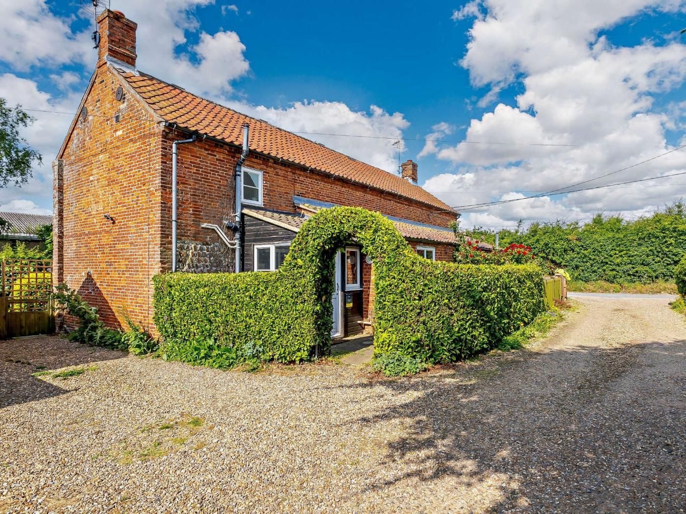 A brick house with a tiled roof, a gravel driveway, and a hedge in front.