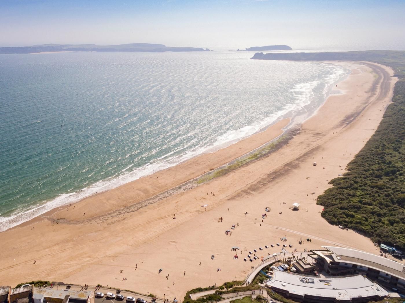A coastal beach with a long stretch of sand, a few people, and a building with a curved roof.
