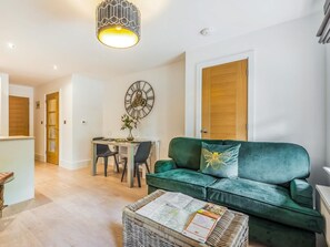A living room with a green sofa, a dining table with chairs, a wall clock, and a hanging light fixture. - 1 Bed in Brockenhurst (oc-87525) (Brockenhurst)