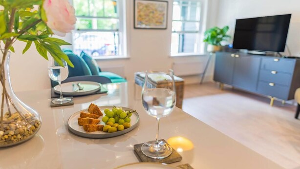 Een eettafel met een schaal druiven en brood, een glas water en een vaas met een bloem.