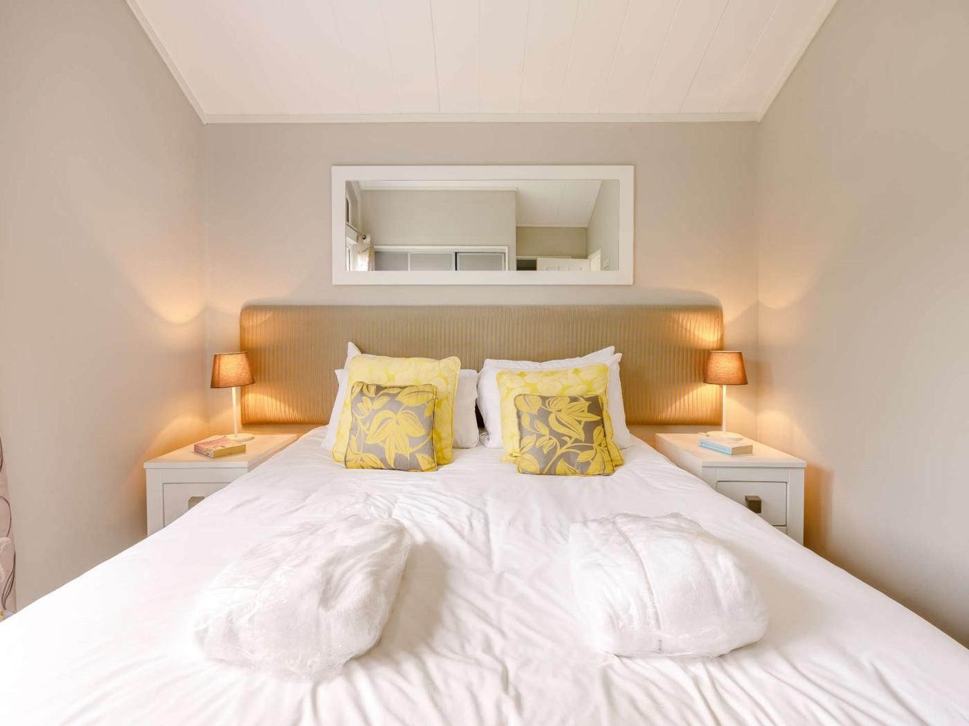 A hotel room with a large bed, two bedside tables, a mirror above the bed, and two lamps on the nightstands.
