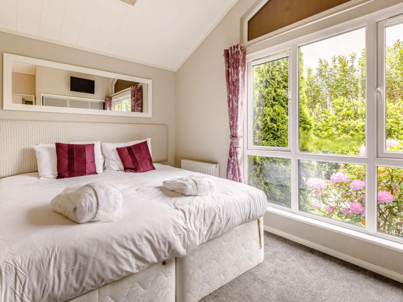 Une chambre d’hôtel avec un grand lit, un miroir au-dessus du lit et une fenêtre donnant sur un paysage verdoyant.