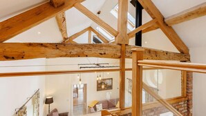 Avoin, loft-tyylinen huone, jossa on näkyvillä olevat puupalkit, lasikatto ja näkymä alapuolella olevalle oleskelutilalle.
