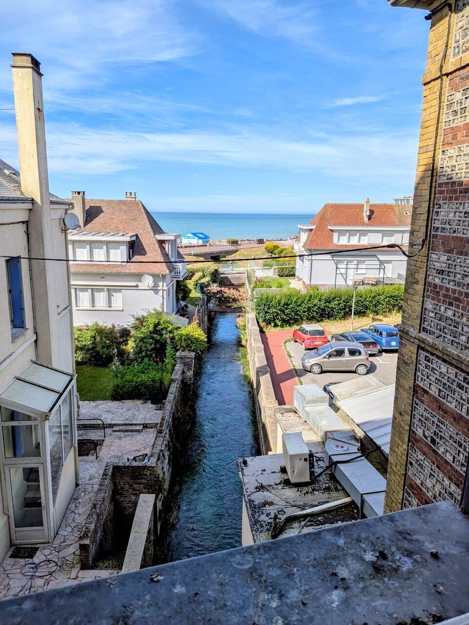 Ein schmaler Kanal zwischen Gebäuden, ein klarer Himmel und ein Blick auf das Meer in der Ferne.