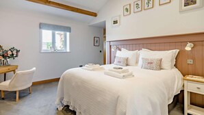 Ein Schlafzimmer mit einem großen Bett, einem Nachttisch, einem Sessel, einem Fenster und Wandbildern.