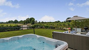 Ein Whirlpool auf einer Terrasse mit Blick auf einen angelegten Garten und einen Zaun.