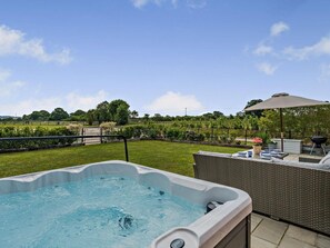 Ein Whirlpool auf einer Terrasse mit Blick auf einen angelegten Garten und einen Zaun.