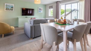 A modern living room with a sofa, dining table, chairs, a flat-screen TV, and large windows. - 2 Bed in Saltash (oc-87715) (Saint Mellion)