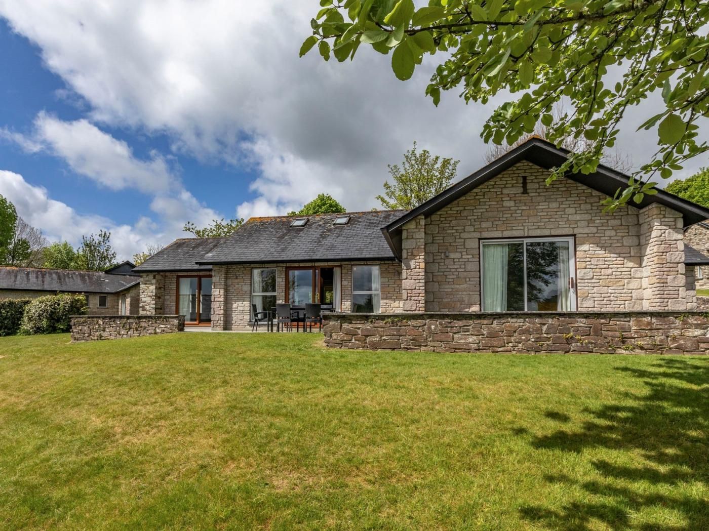 A stone house with a grassy yard, a patio with outdoor furniture, and a large window.