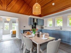 A modern kitchen with blue cabinets, a wooden ceiling, and a dining area with a table set for two. - 3 Bed in Saltash (oc-87718) (Saint Mellion)