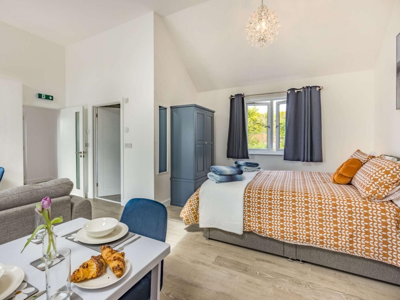 Ein Hotelzimmer mit Bett, einer Essecke mit Tisch und Stühlen, einem Kleiderschrank und einem Fenster mit Vorhängen.