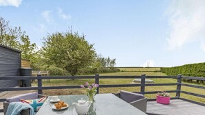 Una veranda esterna con un tavolo in vetro, mobili in vimini e vista su un campo e alberi.