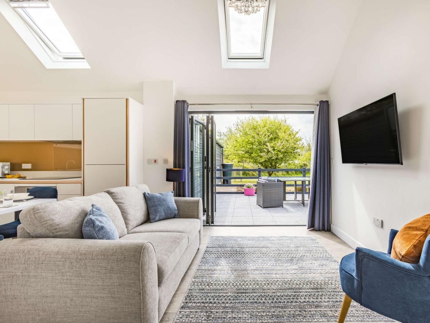 Un salon moderne avec un canapé, un téléviseur et un balcon offrant une vue sur la verdure.
