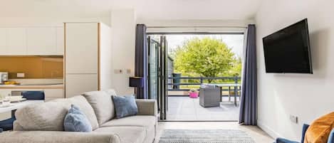 Un salon moderne avec un canapé, un téléviseur et un balcon offrant une vue sur la verdure.