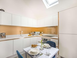 A modern kitchen with white cabinets, a dining table set for two, and a skylight above. - 1 Bed in Bude (oc-87977) (Hersham)