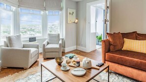 Ein modernes Wohnzimmer mit einer Couch, Sesseln, einem Couchtisch und Blick auf die Stadt durch große Fenster.