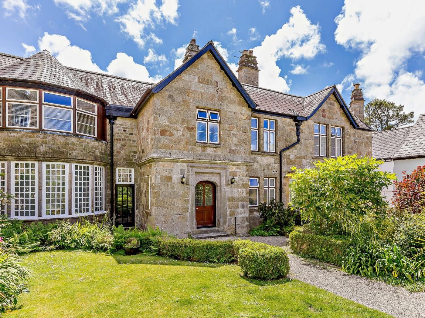 A stone house with a traditional design, featuring a central entrance, multiple windows, and a well-maintained garden.
