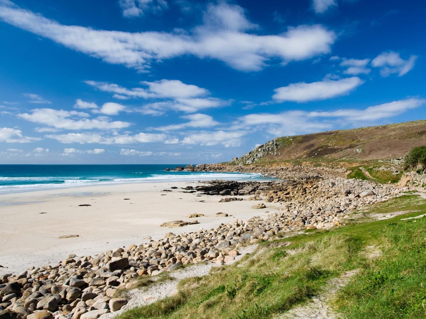 A coastal landscape with a sandy beach, rocky outcrops, and a clear blue sky.