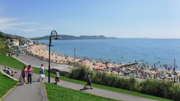 Um calçadão costeiro com uma praia, uma torre do relógio e vista clara do mar.