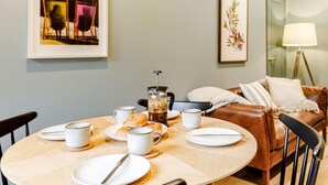 Uma sala de jantar com uma mesa redonda, cadeiras, uma cafeteira e um sofá ao fundo.
