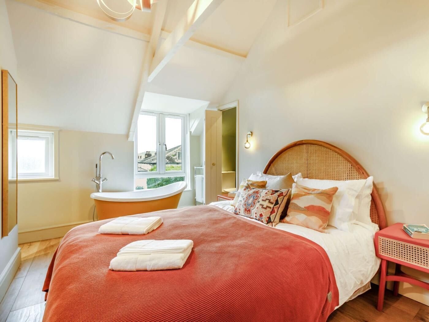 A bedroom with a bed, a red blanket, a wooden headboard, a nightstand, and a window.