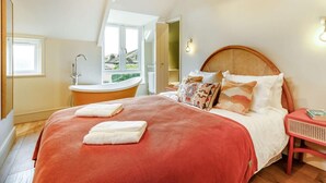 Quarto com cama, manta vermelha, cabeceira de madeira, mesa de cabeceira e uma janela.