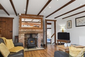 Ein Wohnzimmer mit Kamin aus Ziegelsteinen, Holzbalken, einem Fernseher und einem Sofa.