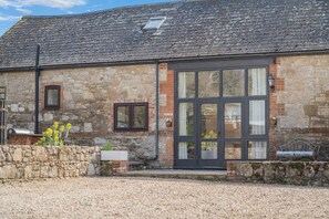 Ein Steinhaus mit einer großen Glasdoor, einem kleinen Fenster und einer Metallbank.