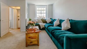 A living room with a teal sofa, a wooden coffee table, a vase with flowers, and a window with a view. - 3 Bed in Budleigh Salterton (oc-88004) (Otterton)