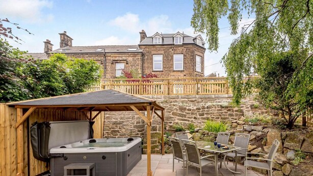 A patio with a hot tub, outdoor seating, and a stone wall. - 4 Bed in Matlock (oc-88011) (Matlock)