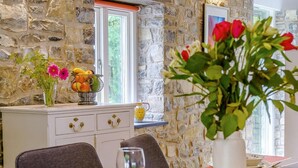 A dining area with stone walls, a white cabinet with drawers, a table set with plates, glasses, and a vase with flowers. - 2 Bed in Cowbridge (oc-88000) (Llandow)