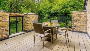 A patio with stone walls, a round table, wicker chairs, and a glass door leading to a garden. - 2 Bed in Cowbridge (oc-88000) (Llandow)